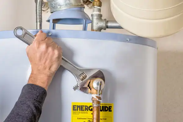 A person uses a wrench to tighten a pipe on a water heater, which has an EnerGuide label.