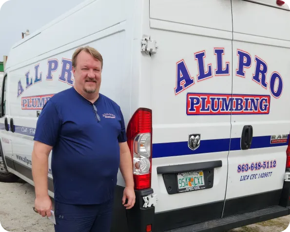 Man in a blue shirt stands next to a white van labeled "All Pro Plumbing.