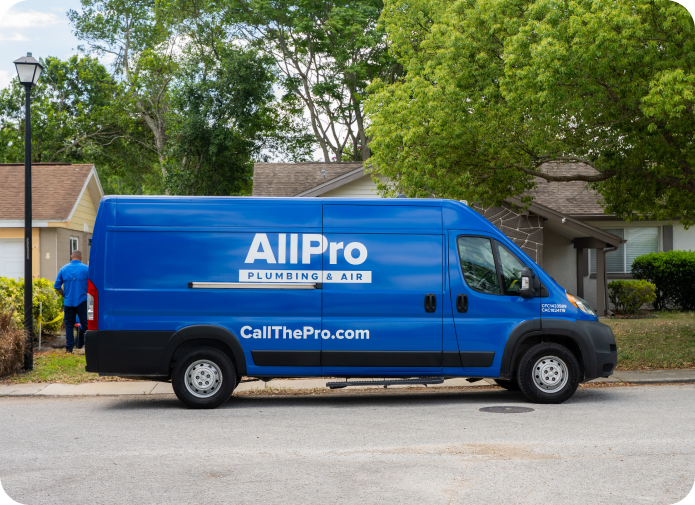 Blue AllPro Plumbing & Air van parked on a residential street, with a person in blue uniform walking toward a house in the background.